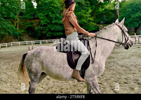 Cheval gris dapple à l'hippodrome par jockey femelle. Femme équestre prenant des leçons d'équitation à l'école de cheval. Dressage de chevaux, dressage de chevaux, trott Banque D'Images