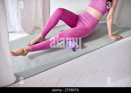 Technique de roulis pour les zones cibles. Masseur à rouleaux en mousse violette étirant les jambes pour la relaxation et renforcer les fessiers, en s'échauffant avant l'exercice. Mince Banque D'Images