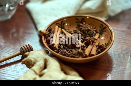 Le bol en céramique à motifs bruns est rempli de bâtons de cannelle, d'anis étoilé et de hanches roses séchées. Une racine de gingembre et une cuillère pour le miel sont à proximité. A se Banque D'Images