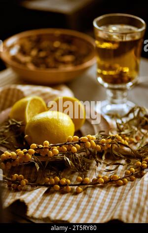 Des brins d'argousier et quelques citrons sont affichés sur une nappe à carreaux. Derrière se trouve une tasse de thé savoureux à l'argousier. Recette de boisson chaude. Banque D'Images