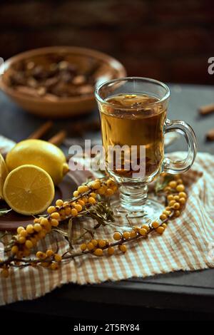 Un verre de thé chaud parfumé à l'argousier entouré de brins d'argousier et de citron sur une nappe à carreaux. Concept de santé et de bien-être. Banque D'Images