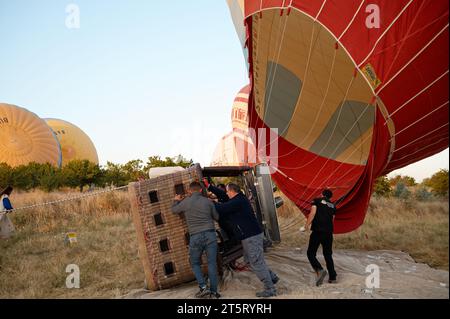 L'équipage allume les brûleurs, soulevant le ballon et le panier en osier pour un voyage au lever du soleil sur les paysages de Cappadoce. Banque D'Images