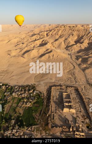 La montgolfière s'élève dans le ciel bleu au-dessus d'un ancien temple de grès érodé et de champs verts Banque D'Images