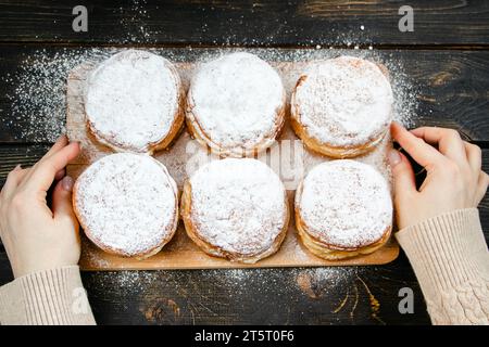 Cuisine traditionnelle Hanukkah sufganiyot.Femme saupoudrer les beignets avec du sucre en poudre.La main tient Berliner avec de la confiture. Banque D'Images