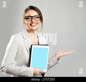 Jeune femme souriante tenant la paume ouverte montrant l'espace de copie pour le nouveau produit ou le texte promotionnel tout en montrant l'écran de la tablette numérique. Vide bleu s Banque D'Images