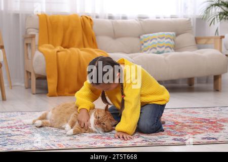 Petite fille caressant chat mignon gingembre sur tapis à la maison Banque D'Images