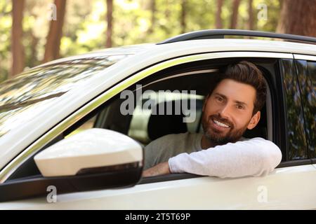 Homme barbu heureux regardant par la fenêtre de la voiture, vue de l'extérieur. Bon voyage Banque D'Images