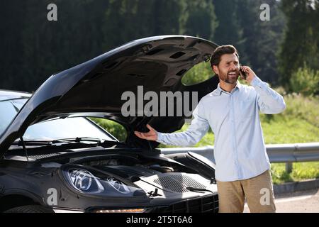 Homme stressé parlant sur smartphone près de la voiture cassée à l'extérieur Banque D'Images