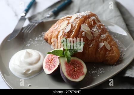 Délicieux croissant avec figue, flocons d'amande et crème sur table blanche, gros plan Banque D'Images