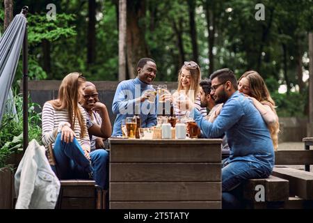 Verres à bière clinquants. Une compagnie d'amis multiculturels célèbre des vacances à l'extérieur en été. Événement de team building de l'entreprise. Pique-nique, barbecue Banque D'Images