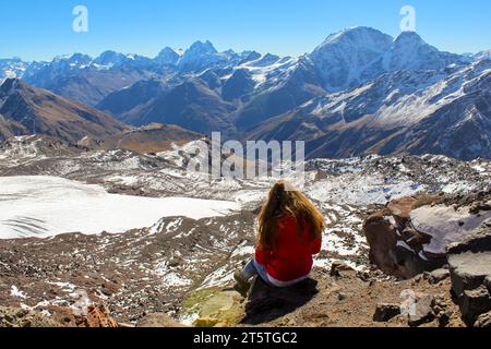 La fille avec les cheveux rouges volant sur le vent assis et profitant de la vue sur la montagne, région du mont Elbrus, Russie. Journée ensoleillée Banque D'Images