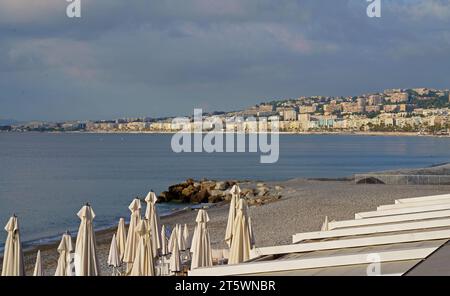 Ambiance matinale et parapluies blancs pliés à Nice, France. Parasols blancs sur la plage contre un ciel bleu clair. Panorama de la plage dans Banque D'Images