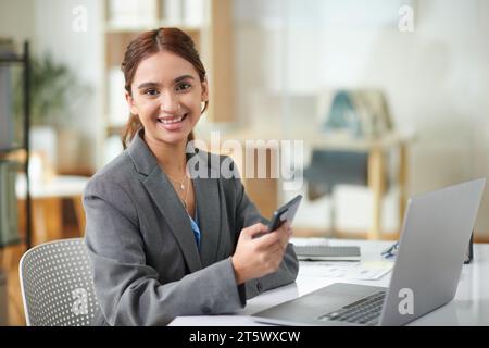 Portrait de jeune femme d'affaires joyeuse avec smartphone à la main assis au bureau Banque D'Images