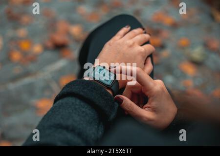 Photo des mains de femme touchant le réglage de la montre intelligente numérique dans le parc l'heure sur l'horloge est 19-00 Banque D'Images