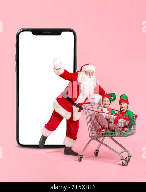 Père Noël et petits elfes avec des cadeaux assis dans le panier et grand smartphone sur fond rose Banque D'Images