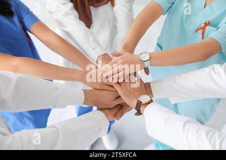 Équipe de médecins avec des rubans rouges mettant les mains ensemble dans la clinique, gros plan. Concept de la Journée mondiale du sida Banque D'Images