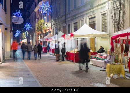 Les gens marchent dans la rue à la recherche de cadeaux de Noël parmi les étals illuminés. Centre historique de Varèse dans la soirée, rue Donizetti Banque D'Images