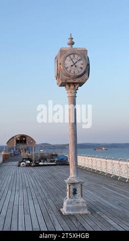 Horloge de tour à l'ancienne sur Mumbles Pier avec la mer en arrière-plan. Journée ensoleillée au début du coucher du soleil avec ciel de couleur pastel. Banque D'Images