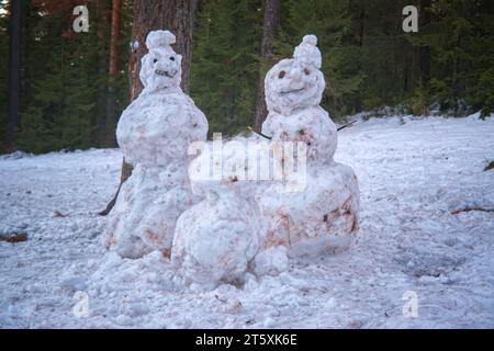 Trois bonhommes de neige dans la forêt sur fond de conifères, gros plan. Famille de bonhommes de neige. Banque D'Images