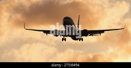 Avion de passagers silhouette. L'avant de l'avion silhouette vole dans le ciel orange avec des nuages, l'avion de passagers atterrit. Avion commercial Banque D'Images