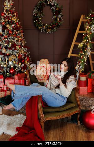 Femme en jeans et pull sitiing sur chaise ouvrant cadeau rouge Banque D'Images