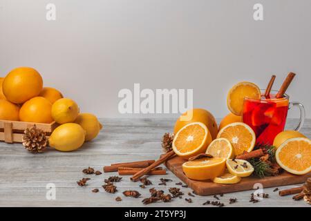 Planche en bois avec des oranges et des citrons, punch dans une tasse en verre, épices, fond clair, salle de copie Banque D'Images