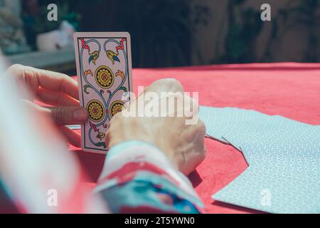 Gros plan et vue arrière des mains d'une femme blanche élégante et méconnaissable qui est assise et tient la carte de tarot dans ses mains, sur la table, espace de copie Banque D'Images