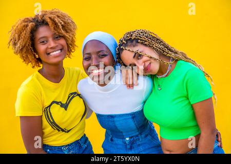 Portrait rapproché de trois femmes de différentes ethnies souriant à la caméra sur fond jaune Banque D'Images