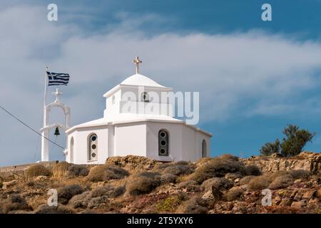 Une chapelle grecque pittoresque se dresse fièrement sur le bord de la falaise, son drapeau flottant dans la brise marine, offrant une vue pittoresque et spirituelle de la Grèce Banque D'Images