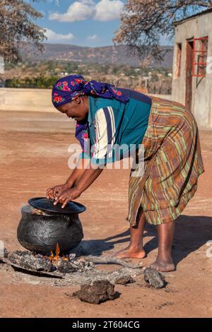 femme africaine faisant bouillir à l'extérieur un setswa de viande sur un pot à trois pattes dans la cuisine extérieure, village en afrique Banque D'Images