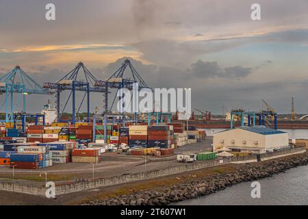 Guatemala, Puerto Quetzal - 20 juillet 2023 : ciel du soir. Grues géantes et beaucoup de boîtes de conteneurs au terminal avec vraquier à l'arrière Banque D'Images