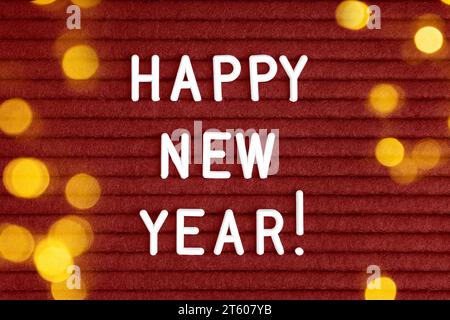 Bonne année, texte sur le panneau de feutre rouge avec des lettres blanches et effet de lumière bokeh . Vue de dessus, pose à plat Banque D'Images
