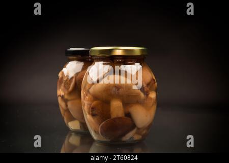 champignons boletus sauvages marinés dans un bocal en verre, isolés sur fond noir. Banque D'Images