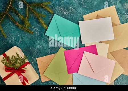 Enveloppes multicolores et boîte cadeau avec ruban rouge près des branches de pin vert sur bleu, Noël Banque D'Images