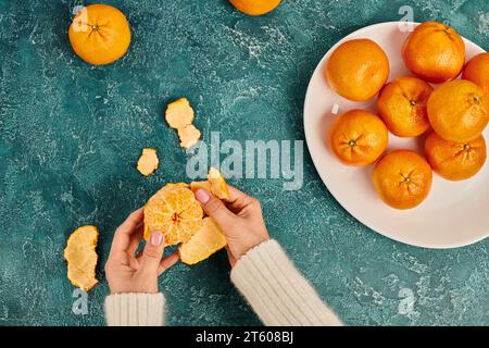 Vue partielle de la femme épluchant la mandarine fraîche mûre sur la surface texturée bleue, concept de Noël Banque D'Images