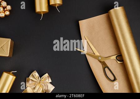 Ciseaux et papier près de l'arc décoratif et des bougies, objets de Noël dorés et brillants sur noir Banque D'Images