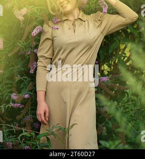 Femme émotive s'amusant à l'extérieur près des fleurs de la Buddleia. Portrait d'une belle blonde sur le coucher de soleil dans la nature. Banque D'Images