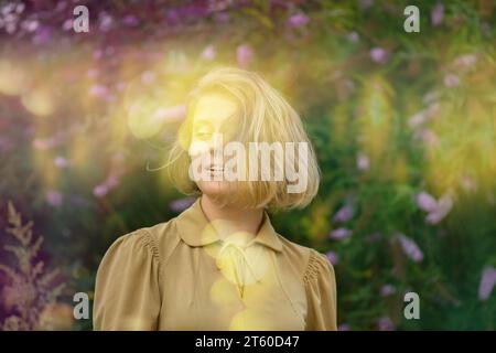 Concept d'émotions heureuses de style de vie. Positive joyeuse jeune femme avec grand sourire regardant joyeusement dans la caméra. Femme près des fleurs de buddleia Banque D'Images