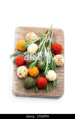 Boules de fromage recouvertes de diverses épices et noix décorées de bâtonnets de romarin isolés sur blanc Banque D'Images