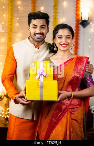 Plan vertical de couple indien souriant heureux avec cadeau pendant le festival diwali en regardant la caméra à la maison - concept de vente de festival, shopping et Banque D'Images