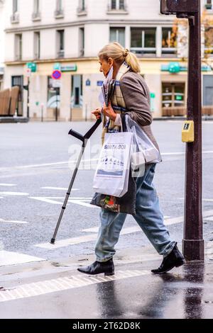 Femme bien habillée avec canne de marche médicale au passage de rue dans le centre-ville - Paris 20, France. Banque D'Images