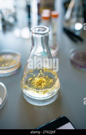 Flacon Erlenmeyer avec échantillon de paillettes dorées mélangé dans un liquide d'analyse sur une table de laboratoire Banque D'Images