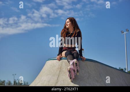 Femme à tête rouge assise sur une rampe de skate dans un skatepark en béton Banque D'Images