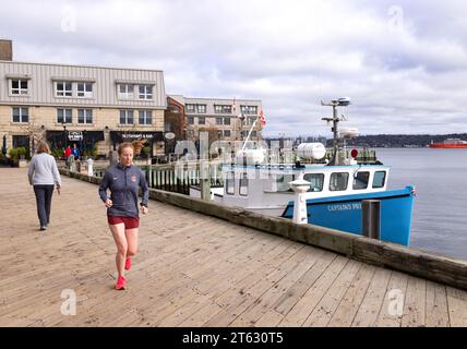 Une femme jogging sur la promenade près du port pour faire de l'exercice matinal ; Halifax Nova Scotia Canada. Mode de vie sain Banque D'Images