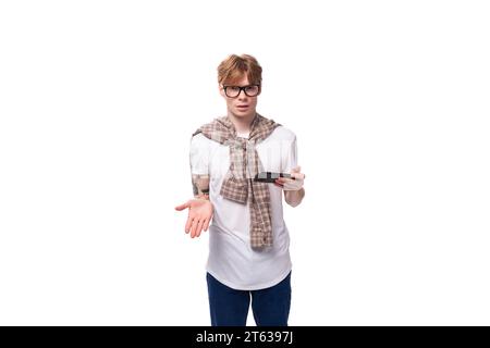 jeune homme caucasien aux cheveux roux dans une chemise utilise activement un smartphone Banque D'Images