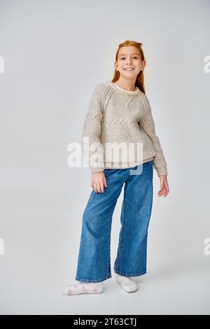 mignonne fille préadolescente dans la tenue élégante d'hiver posant sur fond gris souriant à la caméra, la mode Banque D'Images