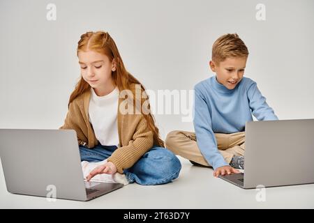 mignons enfants préadolescents dans des tenues à la mode sur le sol regardant leurs ordinateurs portables, concept de mode Banque D'Images