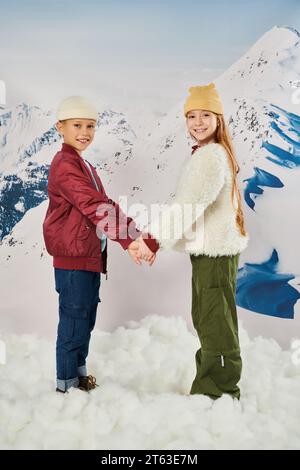 mignons amis préadolescents dans des vestes d'hiver élégantes et des chapeaux de bonnet tenant les mains et souriant à l'appareil photo Banque D'Images