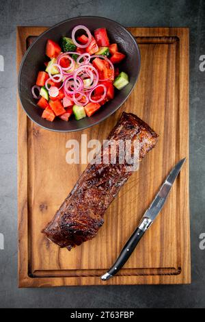 steak bien cuit avec salade de tomates et concombres sur un plateau en bois, vue de dessus Banque D'Images