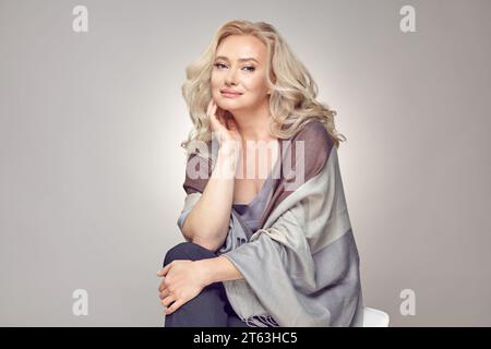 Femme âgée mature portant dans Tippet plaid assis sur une chaise sur gris isolé. Banque D'Images
